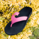 Auf dem Foto sieht man einen unserer individuellen Flip-Flops. Die Sohle ist schwarz, mit einem pinken Streifen in der Mitte und der Zehensteg ist ebenfalls pink. Der Flip-Flop steht in einem Busch mit gelben Blüten, um ein Frühlingsgefühl zu erwecken.
